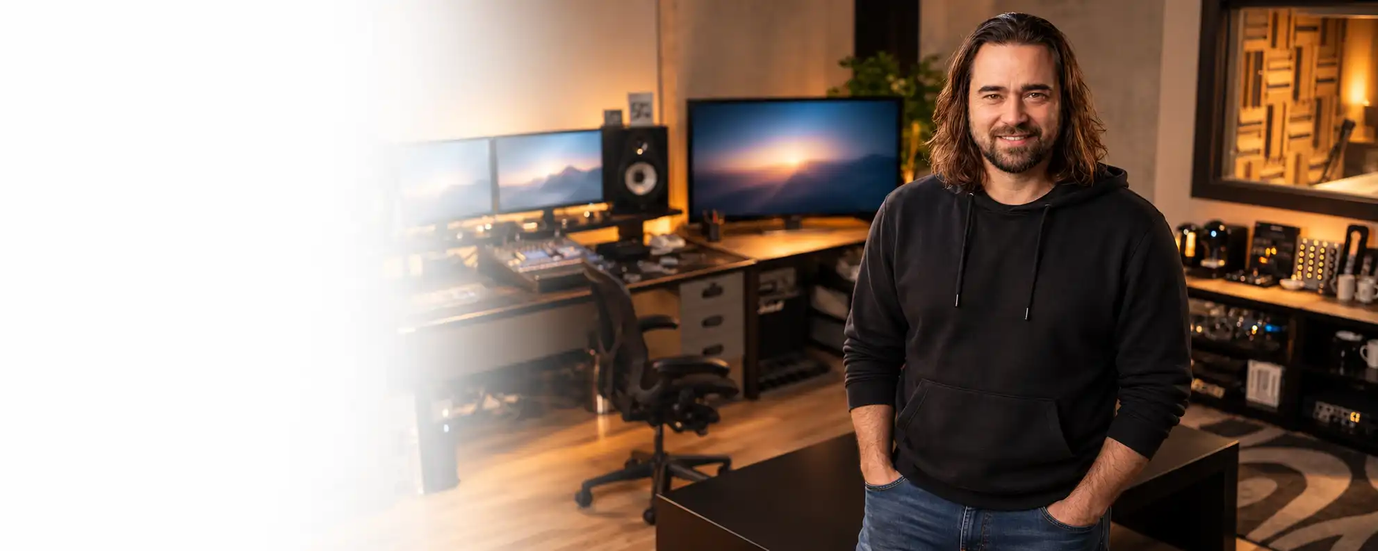 A professional audio studio control room with a seated person, mixing equipment and warm lighting.